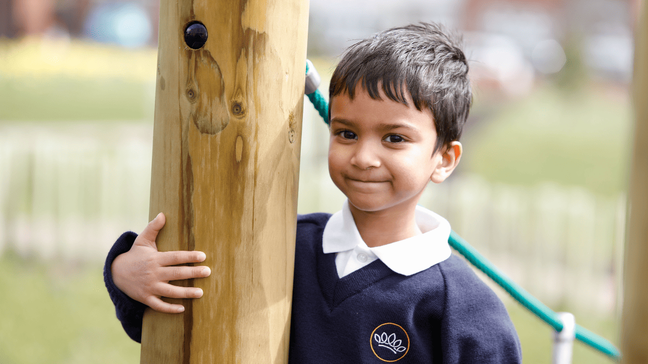 Image of pre school pupil at Crown Street Primary School smiling on the climbing frame outside.